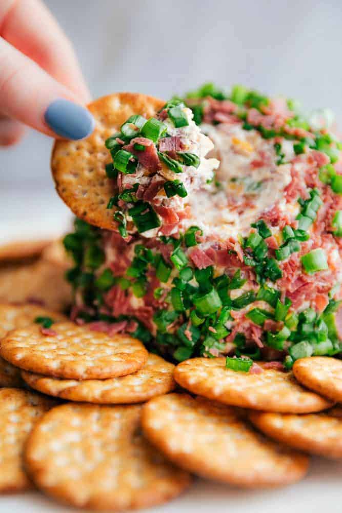 Chipped beef cheese ball with a hand dipping a cracker into it. 