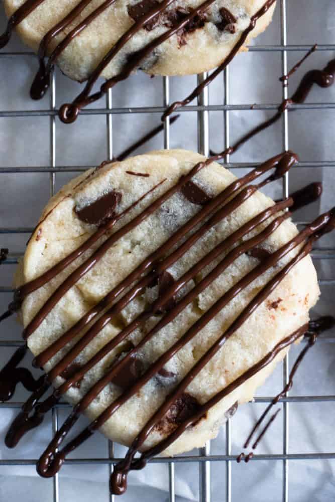 Chocolate chip shortbread cookies on a cooling rack with chocolate being drizzled over top.