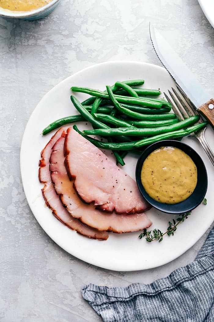Ham sliced on a plate with green beans and honey mustard sauce.
