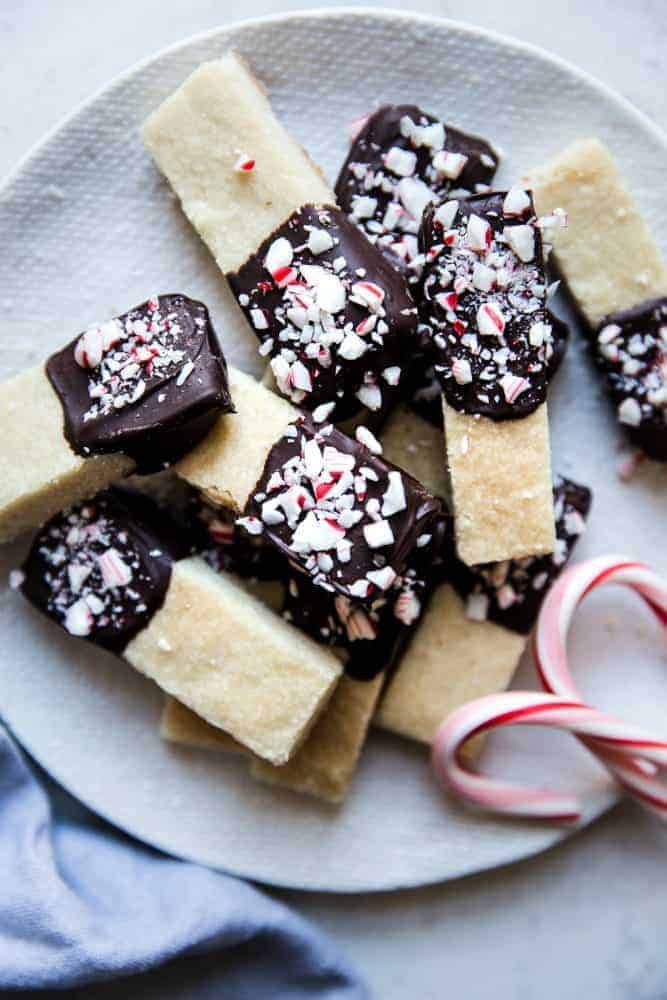 Close up photo of chocolate peppermint dip shortbread cookies on a white plate with two candy canes on the side.