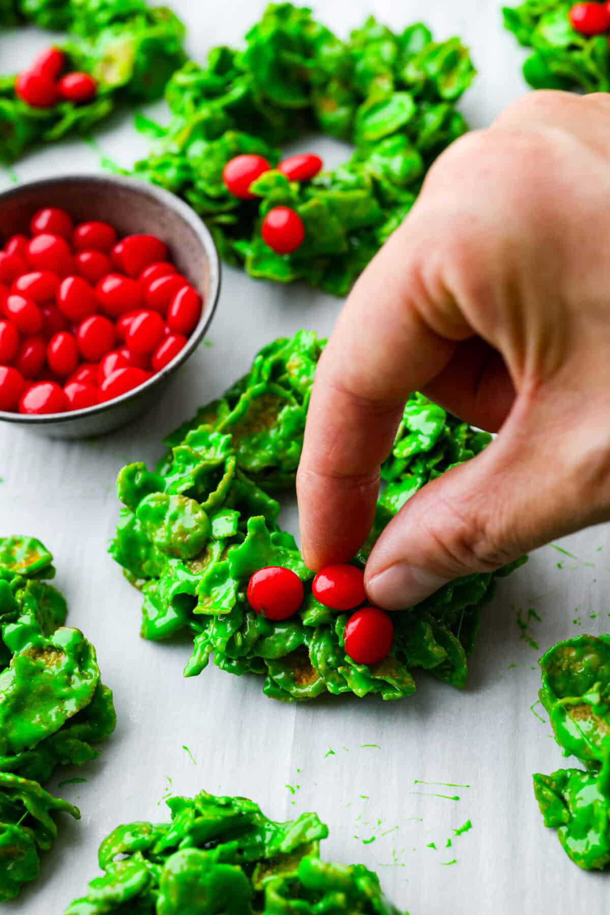 Close up shot of someone placing the cinnamon candies onto the Christmas cornflake wreaths. 