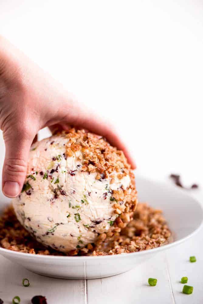 Cranberry pecan cheese ball being rolled and pecans.