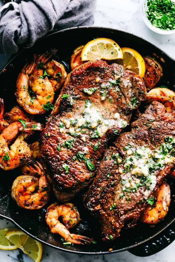 Steak and shrimp resting in a cast iron pan with garlic butter on top of the steak.