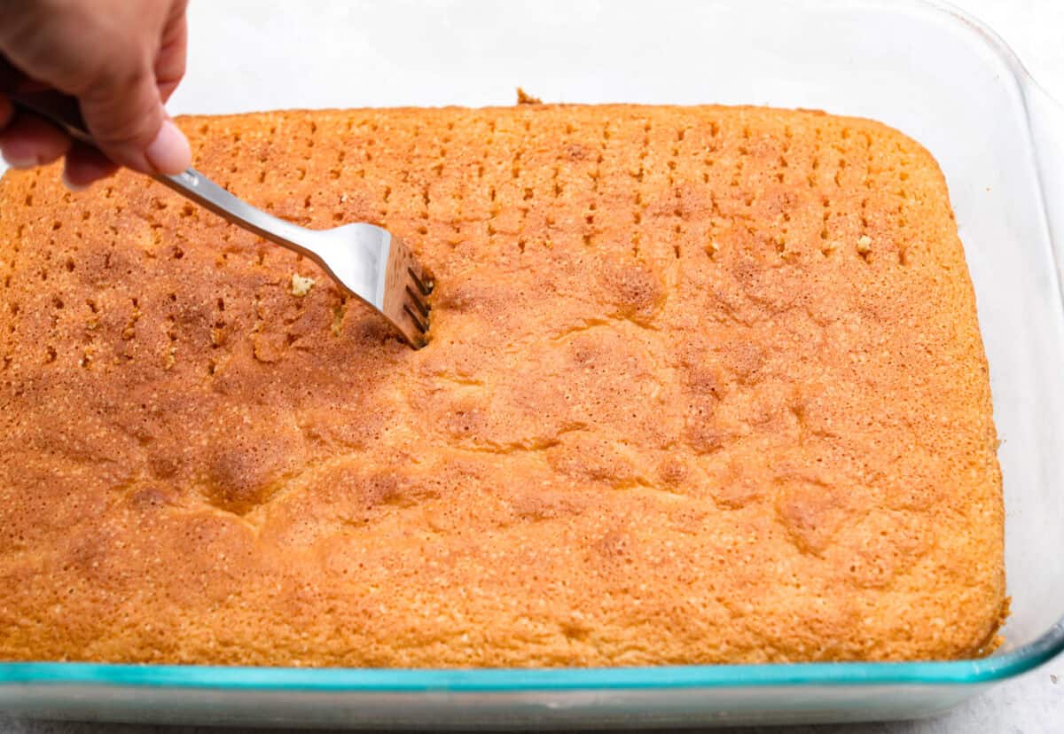 Angle shot of someone poking the tres leches cake repeatedly with a fork. 