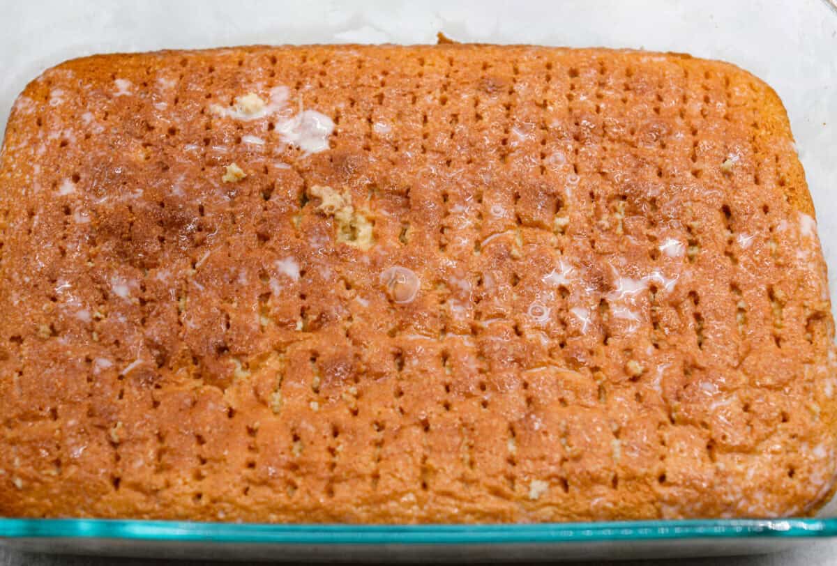 Angle shot of the cake with fork pokes and milk mixture poured over the top. Making it a tres leches cake. 