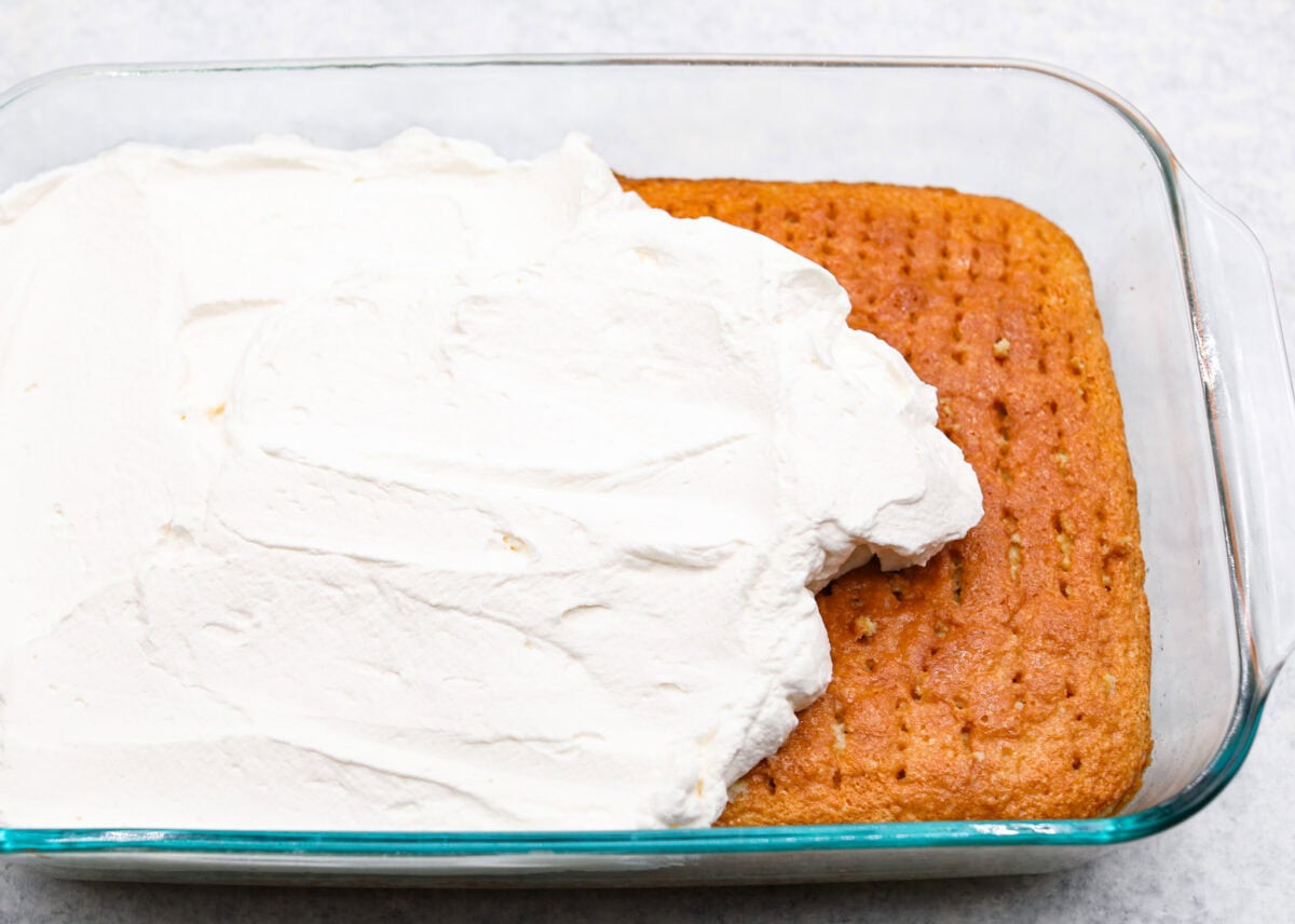 Angle shot of the whipped cream topping being spread over the tres leches cake. 