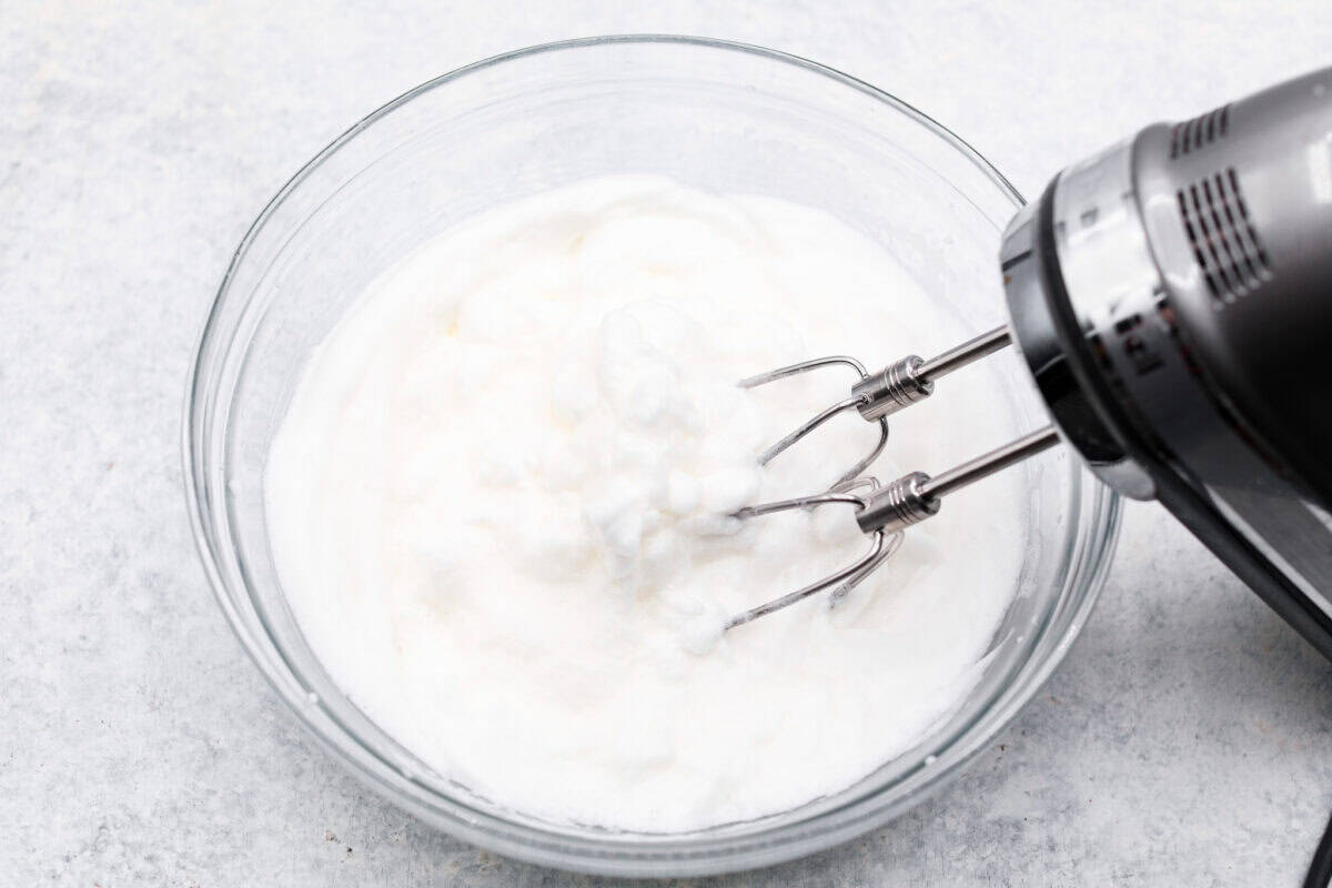 Overhead shot of egg whites being whipped in a glass bowl with a hand mixer. 