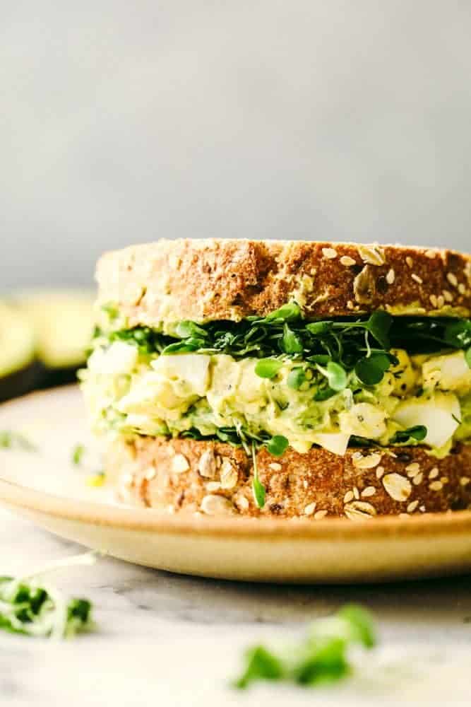 Avocado egg salad on a sandwich on a plate.