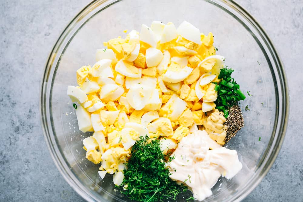 Ingredients for egg salad in a clear glass bowl.