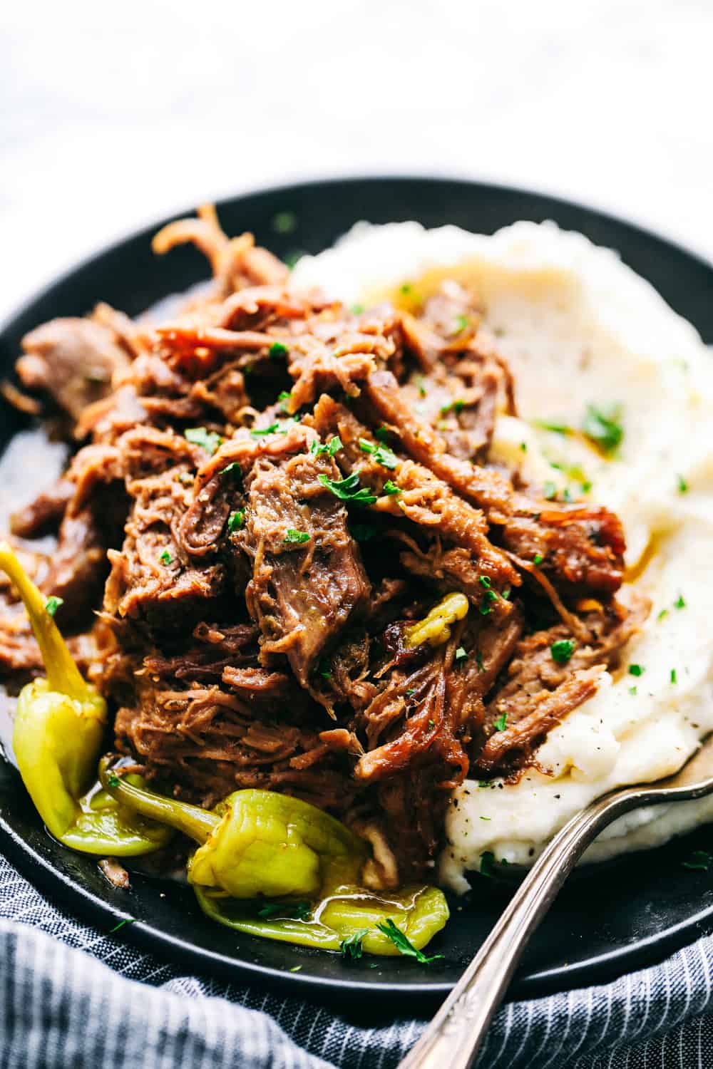 Slow Cooker Mississippi Pork Roast is a savory, sweet and spicy pork roast that is tender to the touch and falls apart with ease. It takes minutes to prepare and can be paired with a variety of sides. Your family will fall in love with this incredibly flavorful, melt in your mouth pork roast! Pork roast on a plate with mashed potatoes.