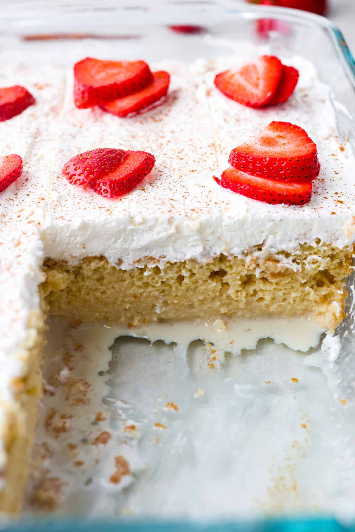 Close up shot of tres leches cake with a piece taken out of it so you can see the milk mixture seeping out of the bottom of the cake. 