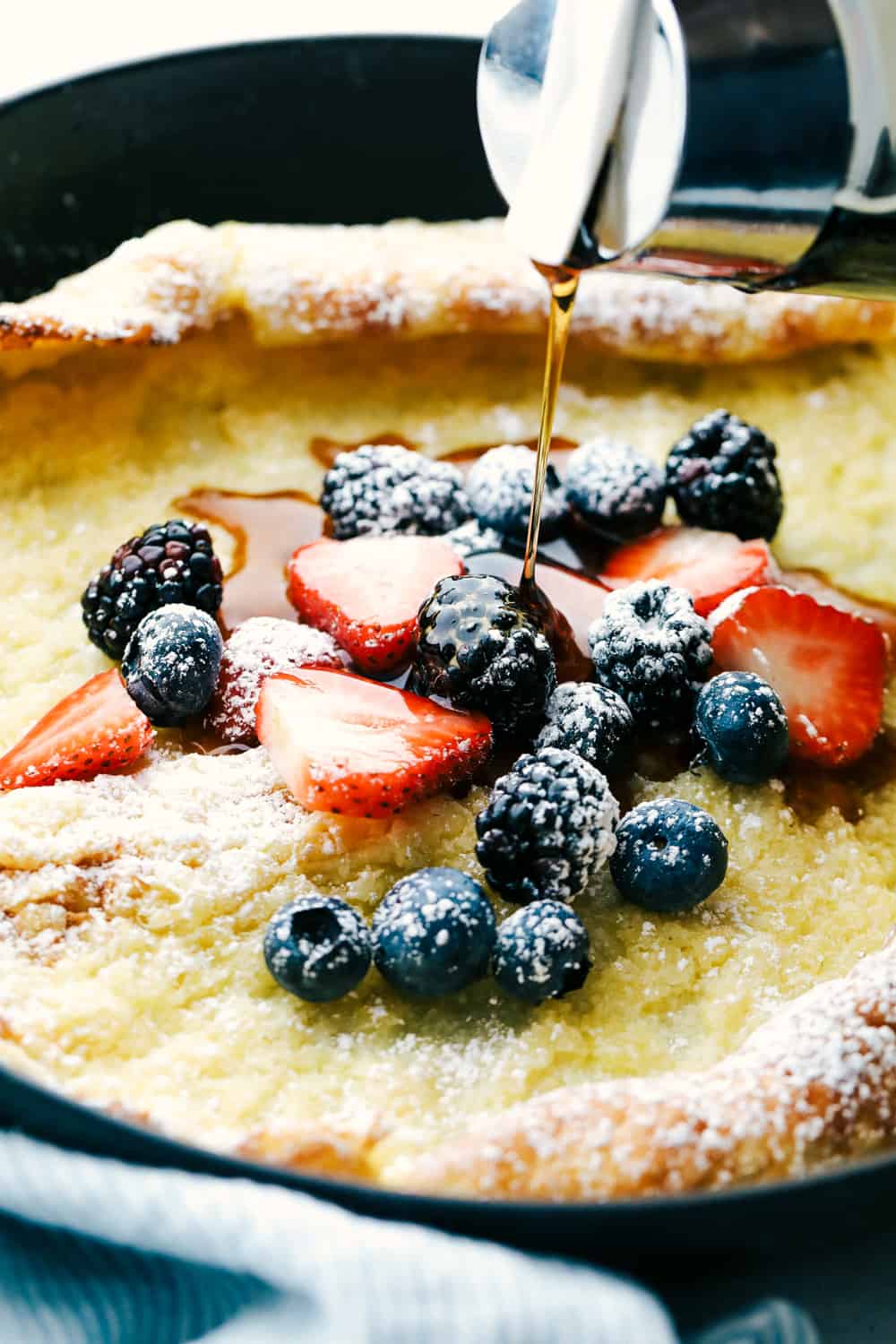 German over pancake with fruit and syrup being poured overtop. 