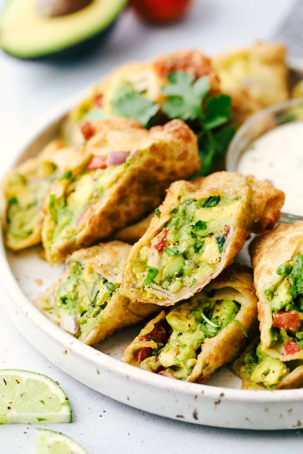 Avocado Egg Rolls in a stack on a plate with dip.