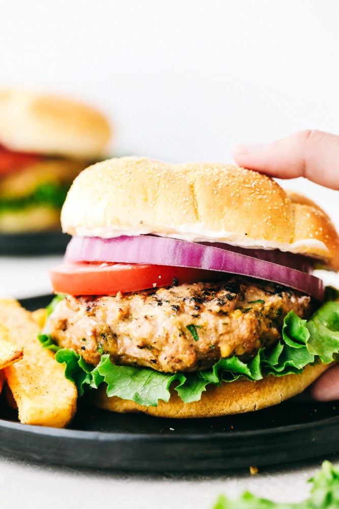 Hamburguesa de pavo en un bollo con cebolla roja, tomates y papas fritas en el lateral. 