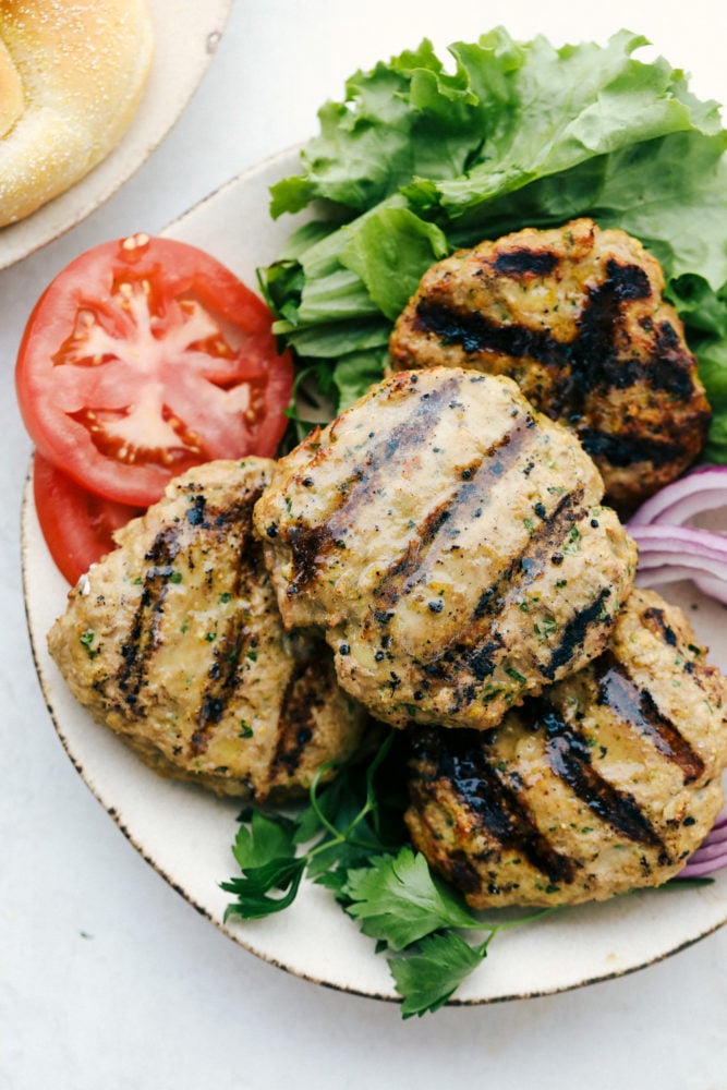 Grilled turkey burgers on a plate with lettuce, tomatoes and onions. 