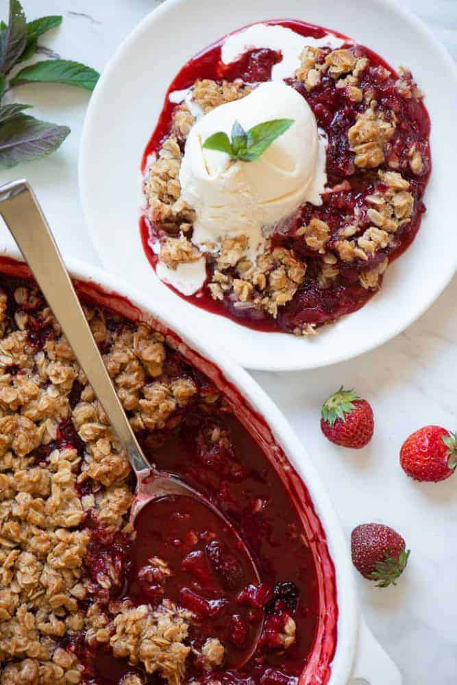 Strawberry Rhubarb Crisp in a white dish with a serving on a small white plate topped with ice cream.