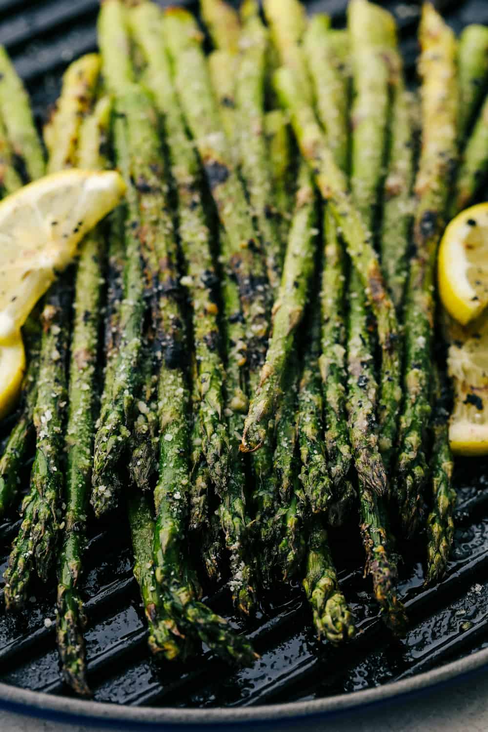 Asparagus on the grill plate with lemon wedges on the side.