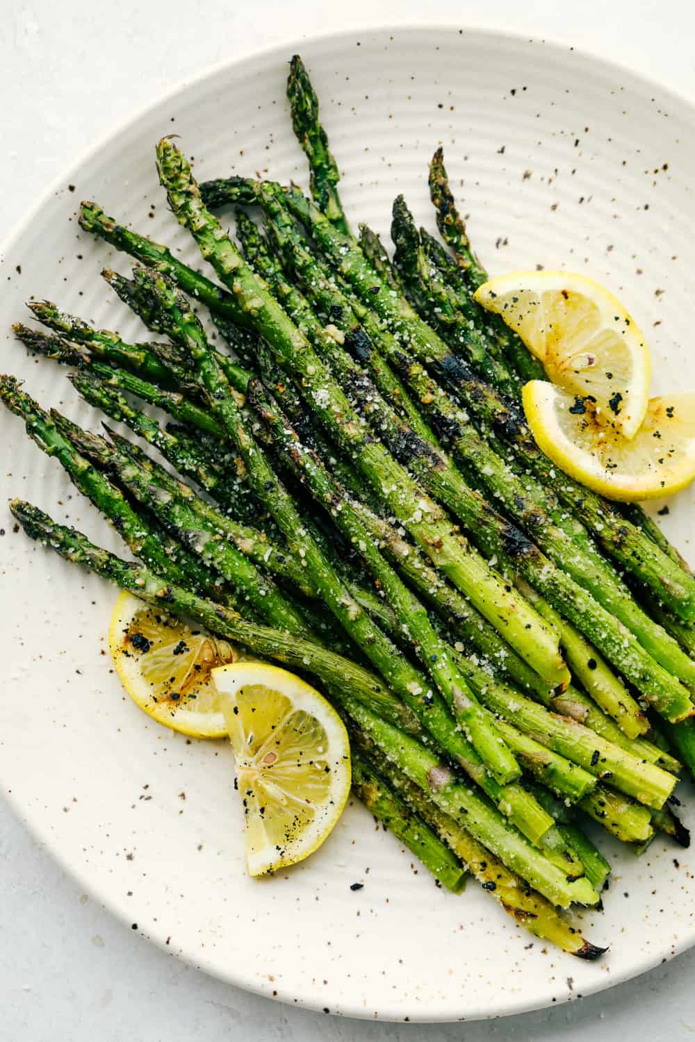 Grilled Asparagus on a white plate garnished with lemon wedges. 