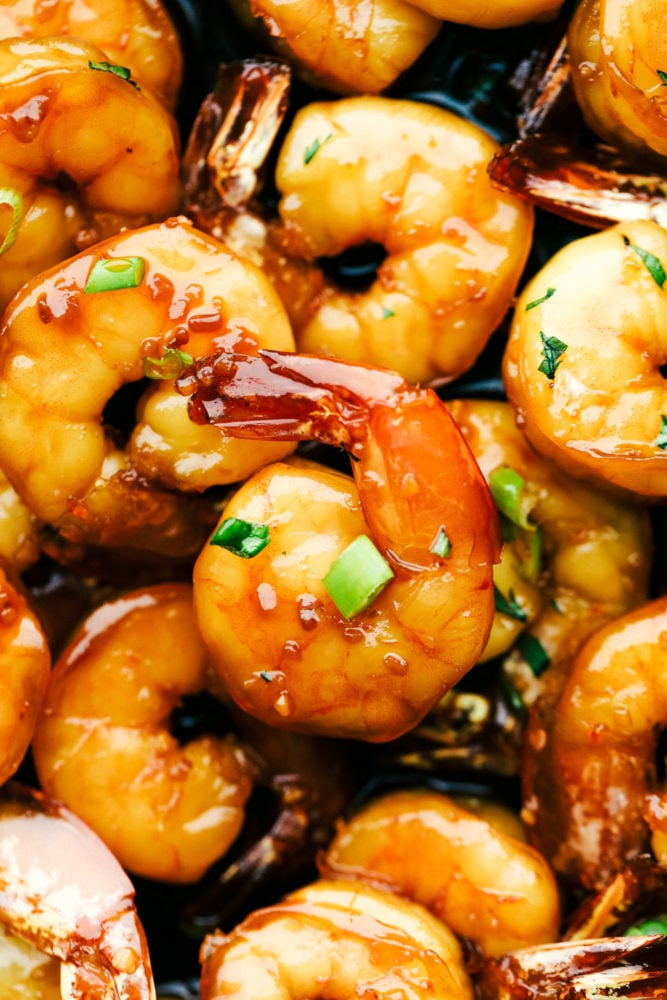 Sticky honey garlic butter shrimp up close with green onions garnished over top. 
