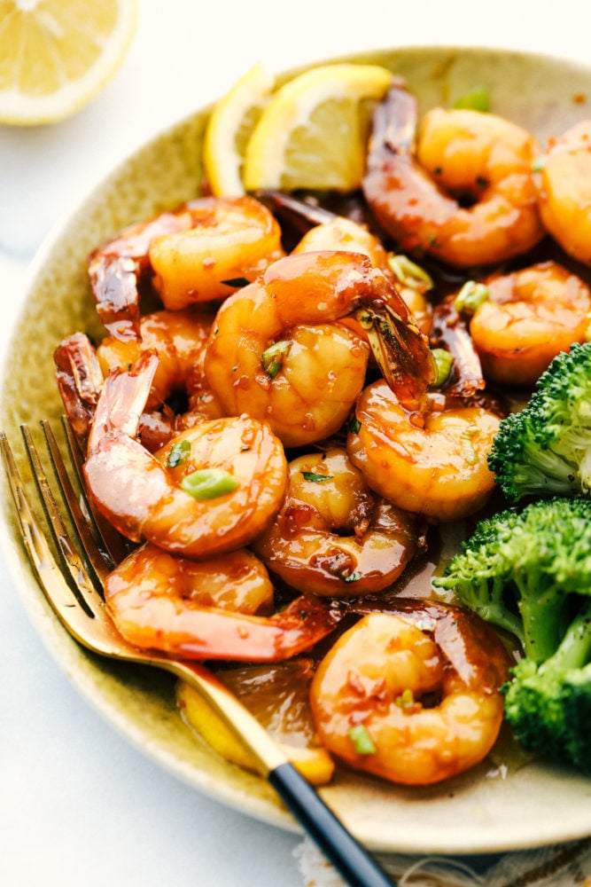 Sticky honey garlic butter shrimp on a plate with broccoli and lemon garnishes. 