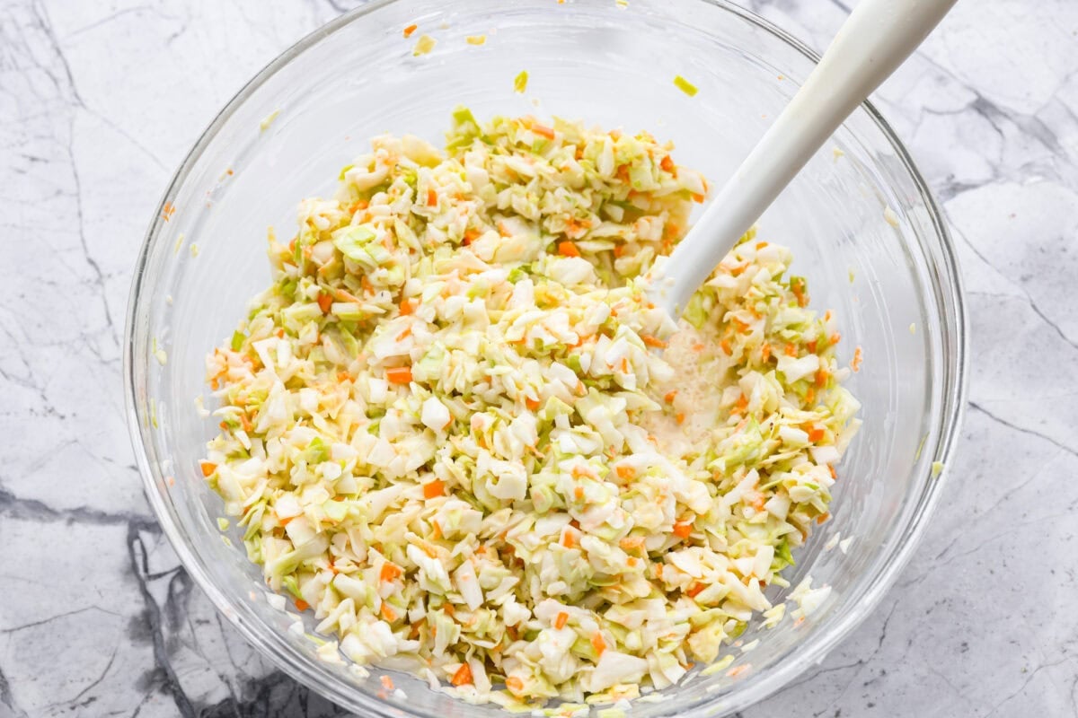 Cabbage mixture and dressing being stirred together. 