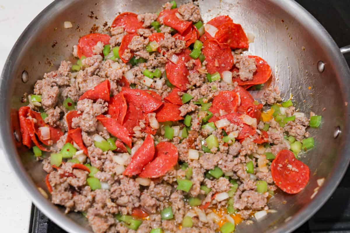 Overhead shot of sausage, onions, peppers and pepperoni cooking in a skillet. 