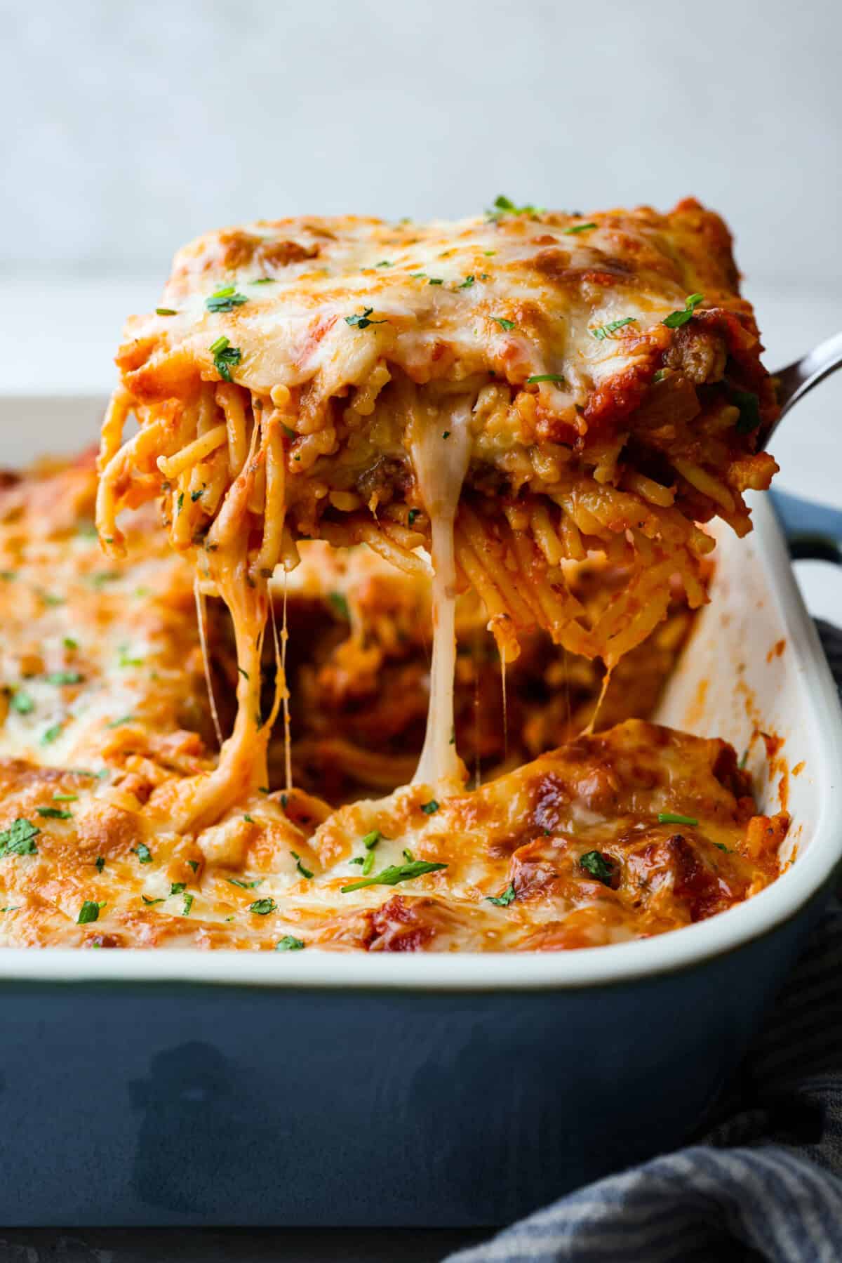 Side shot of someone lifting a piece of baked spaghetti out of the pan. 