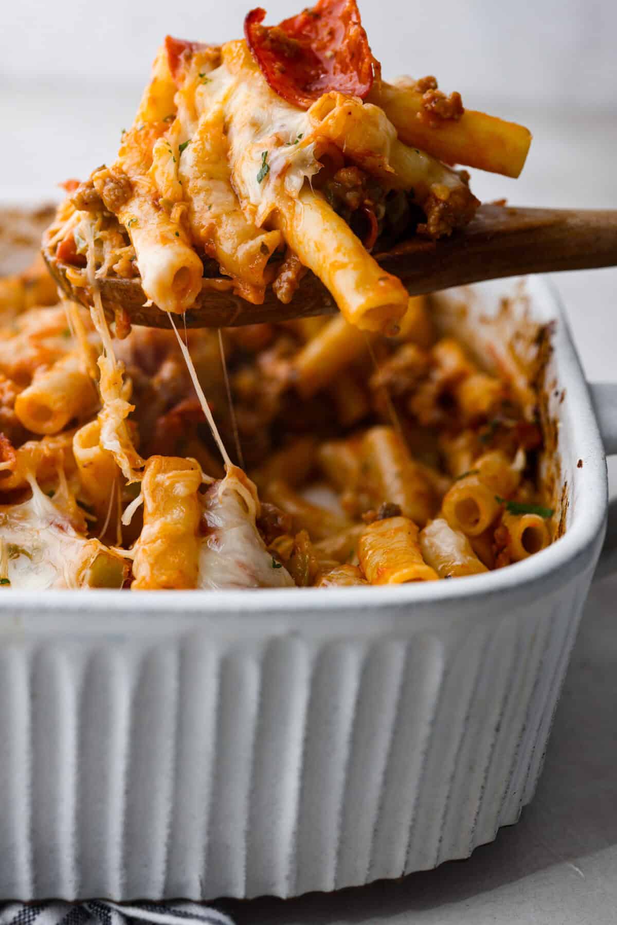 Side shot of someone scooping a portion of cheesy baked ziti out of a baking dish. 