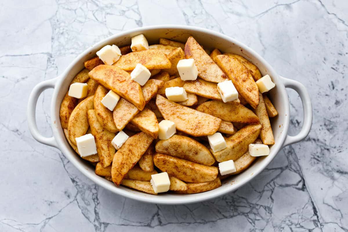 Overhead shot of the cinnamon sugar coated apples in a baking dish with squares of butter spread out on top. 