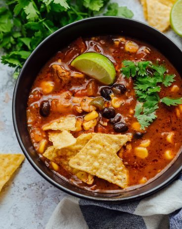 Chicken tortilla soup served in a black bowl with toppings