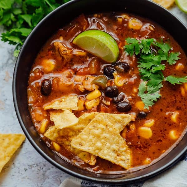 Chicken tortilla soup served in a black bowl with toppings