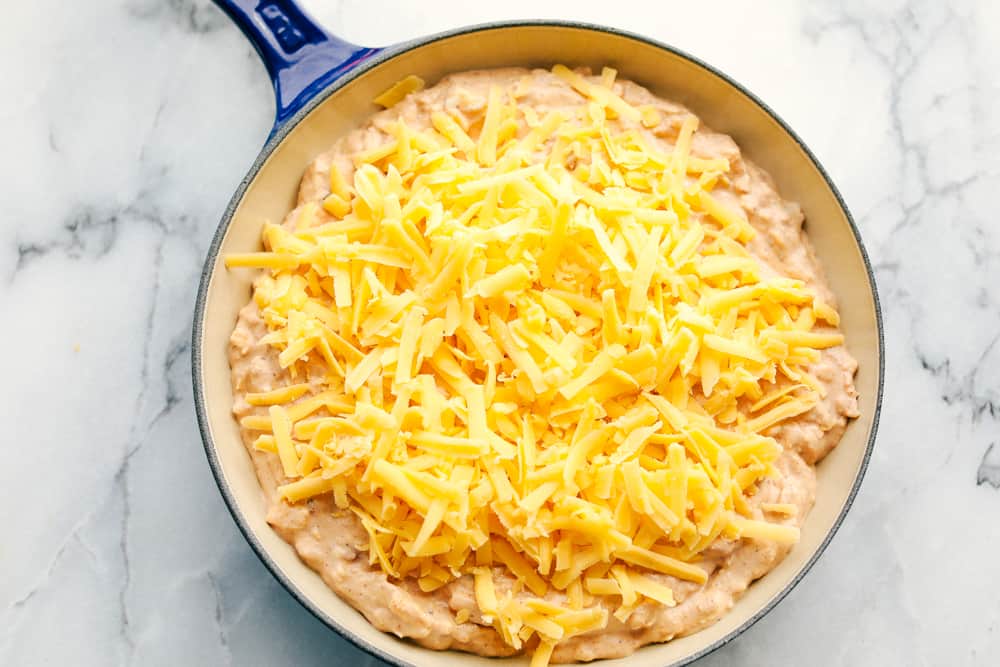 bean dip mixture with cheese on top in the cast iron pan ready to go in the oven