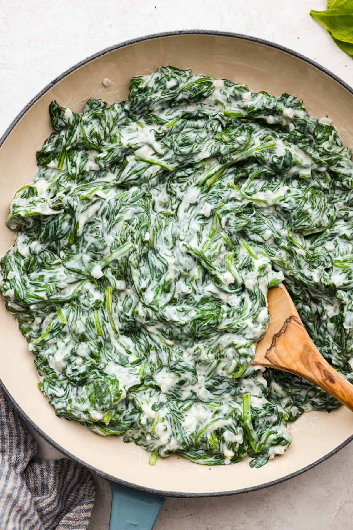 Top close view of creamed spinach in a serving bowl with a wood spoon.