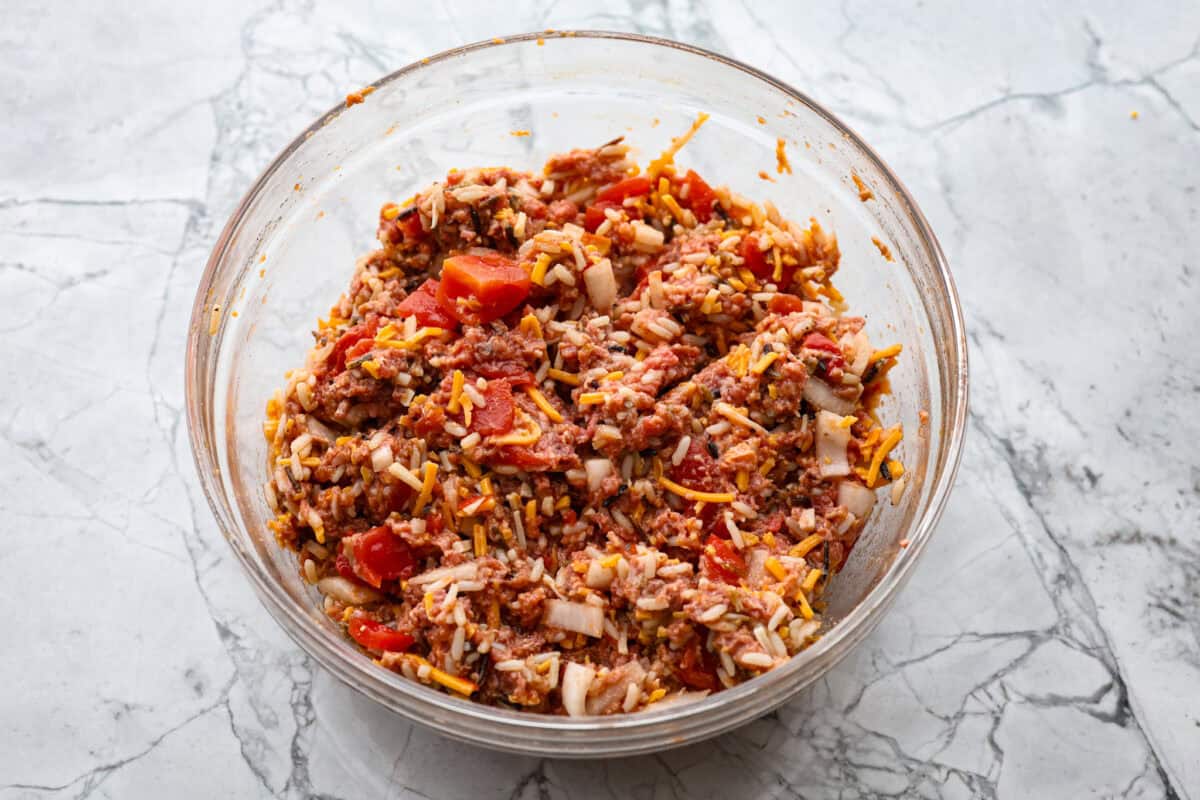 Overhead shot of meat, cheese, diced tomatoes, onion, rice, seasonings and cheese mixture.