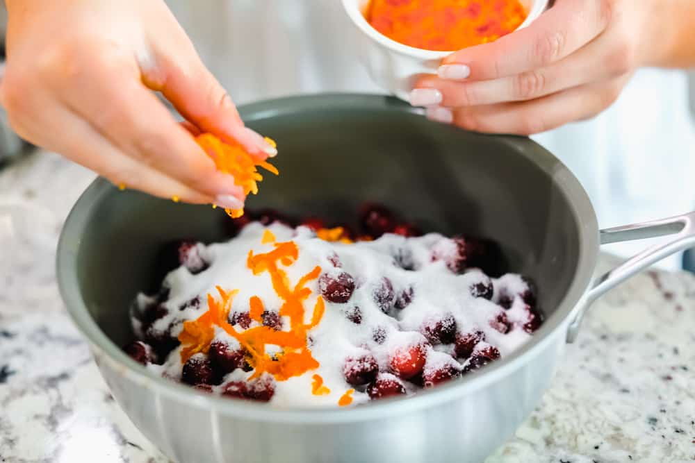 Cranberries in a pan with sugar and adding orange zest overtop 