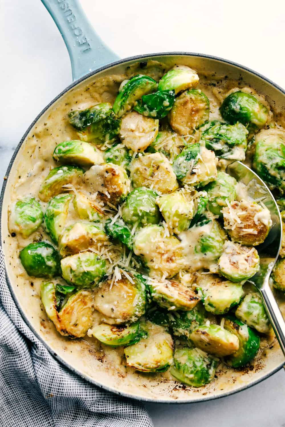 Top view of creamy parmesan garlic Brussels sprouts in a skillet with a silver serving spoon.
