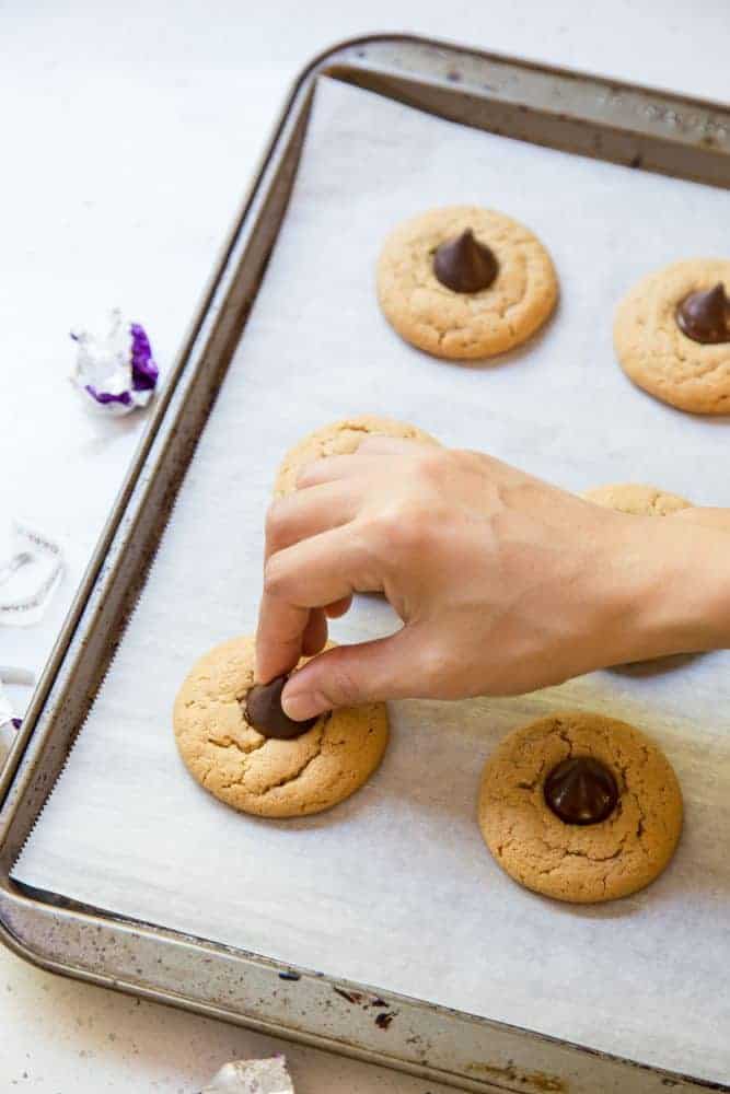 Adding chocolate kisses to peanut butter blossom cookies