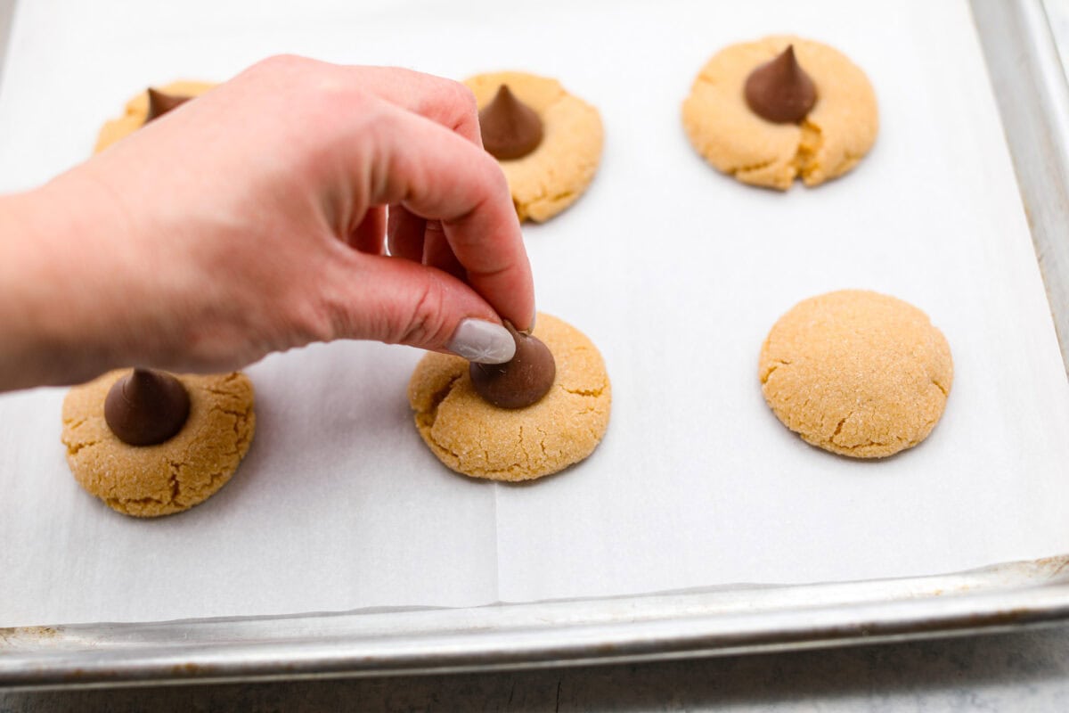 Angle shot of someone placing a Hersheys Kiss in the center of a baked cookie dough ball. 