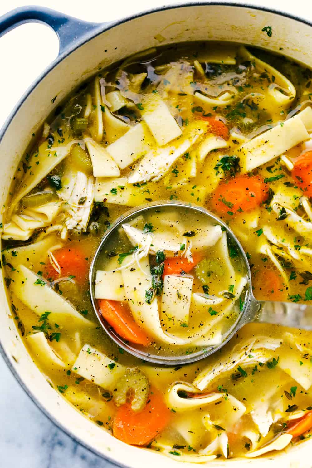 Top view of chicken noodle soup in a pot with a ladle.