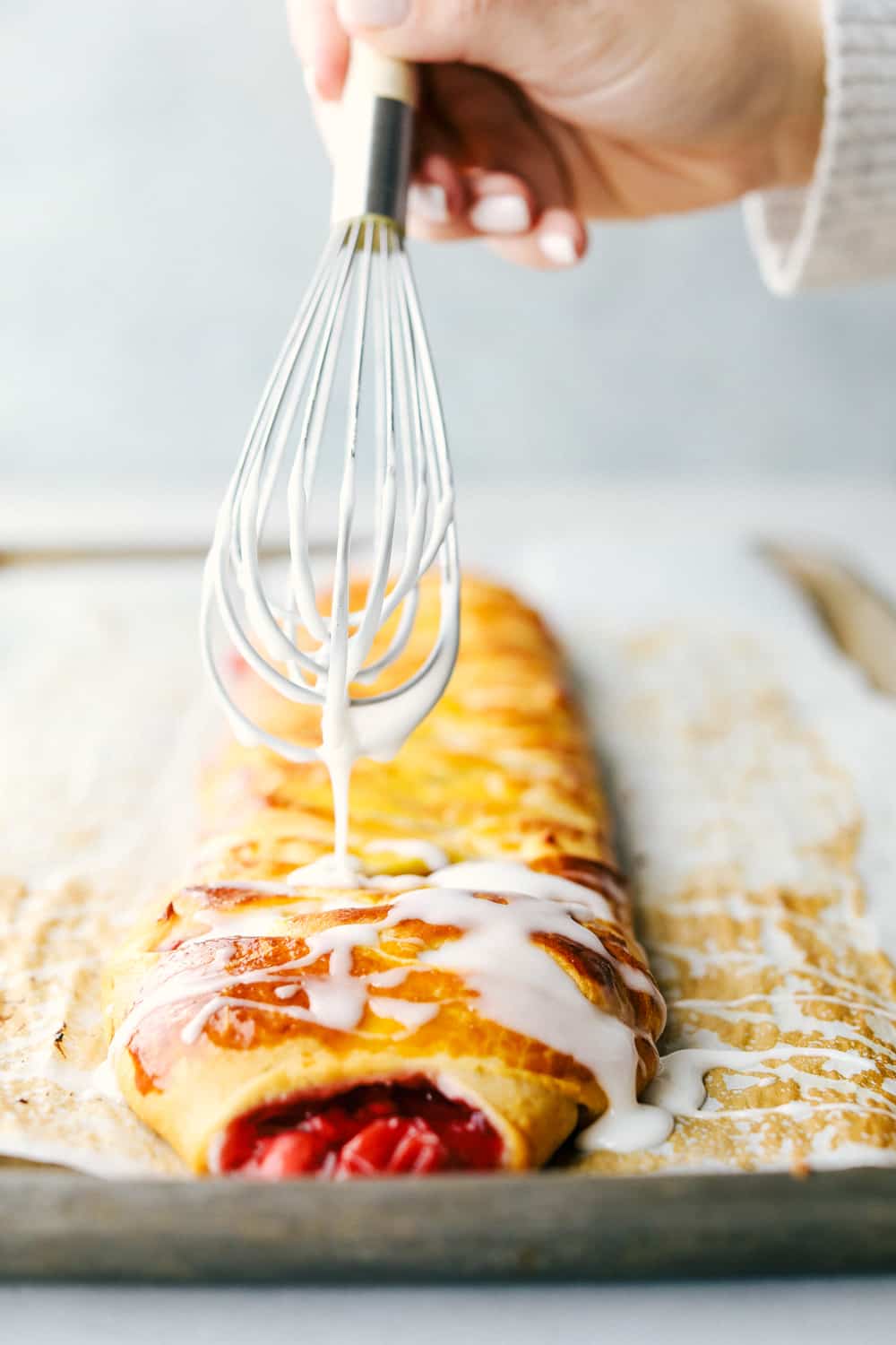 Drizzling glaze with a whisk over the cherry almond cream cheese breakfast braid