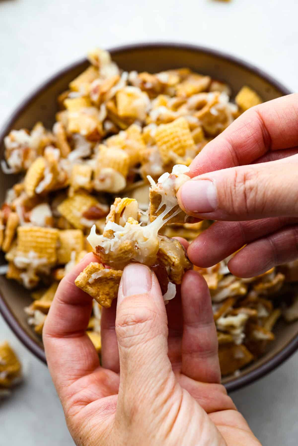 Close up shot of someone stretching a chunk of ooey gooey Chex mix between their fingers. 