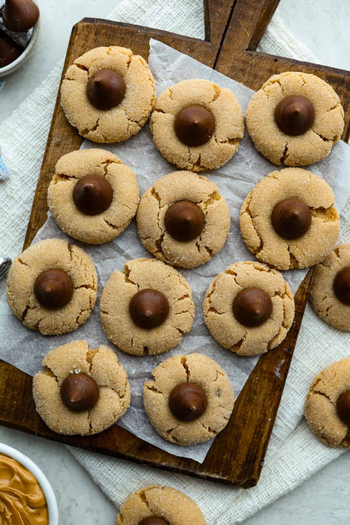 Overhead shot of baked peanut butter blossom cookies on a wooden cutting board. 