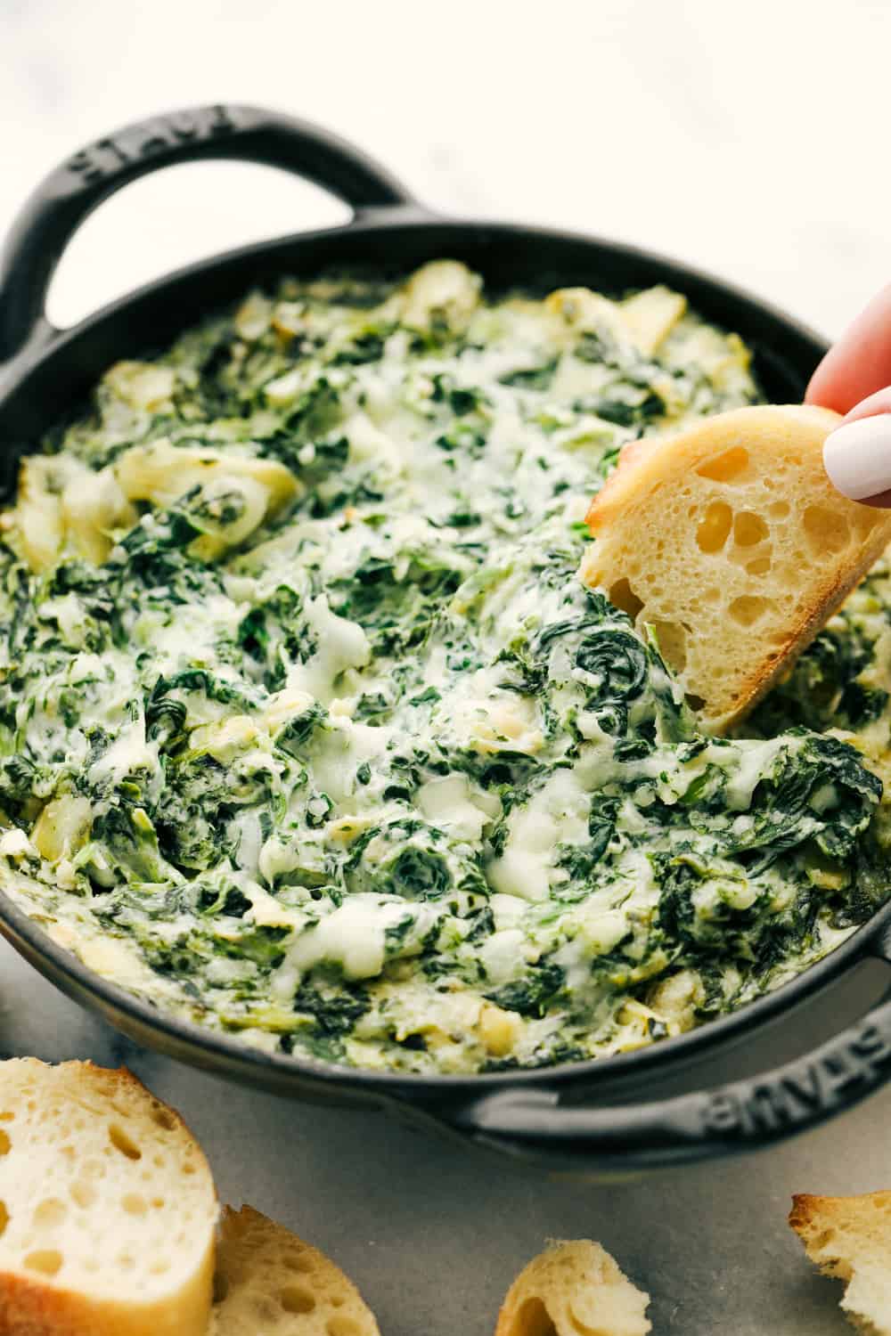 Spinach artichoke dip with bread dipped inside it.