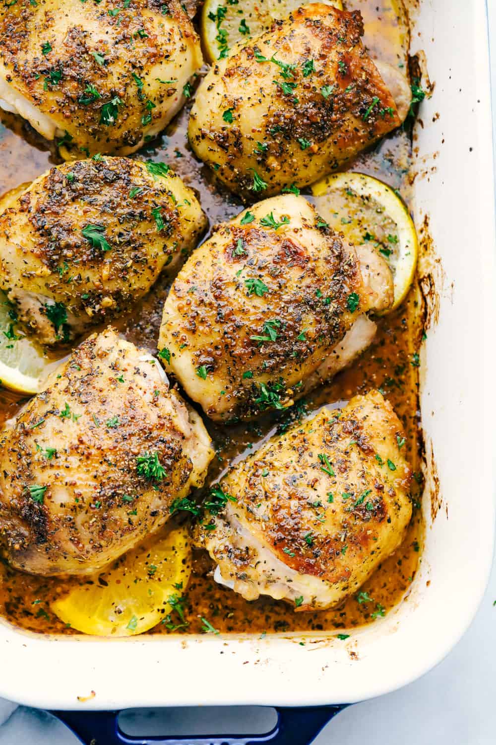 Baked chicken thighs in a baking dish covered in a glaze sauce with lemon slices.