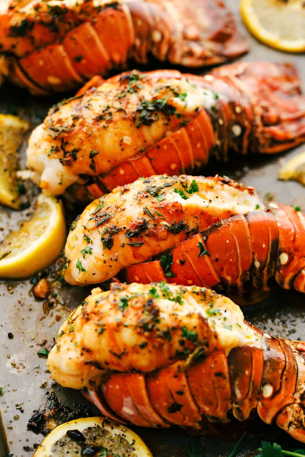 Lobster tails broiled on a sheet pan with lemon slices. 