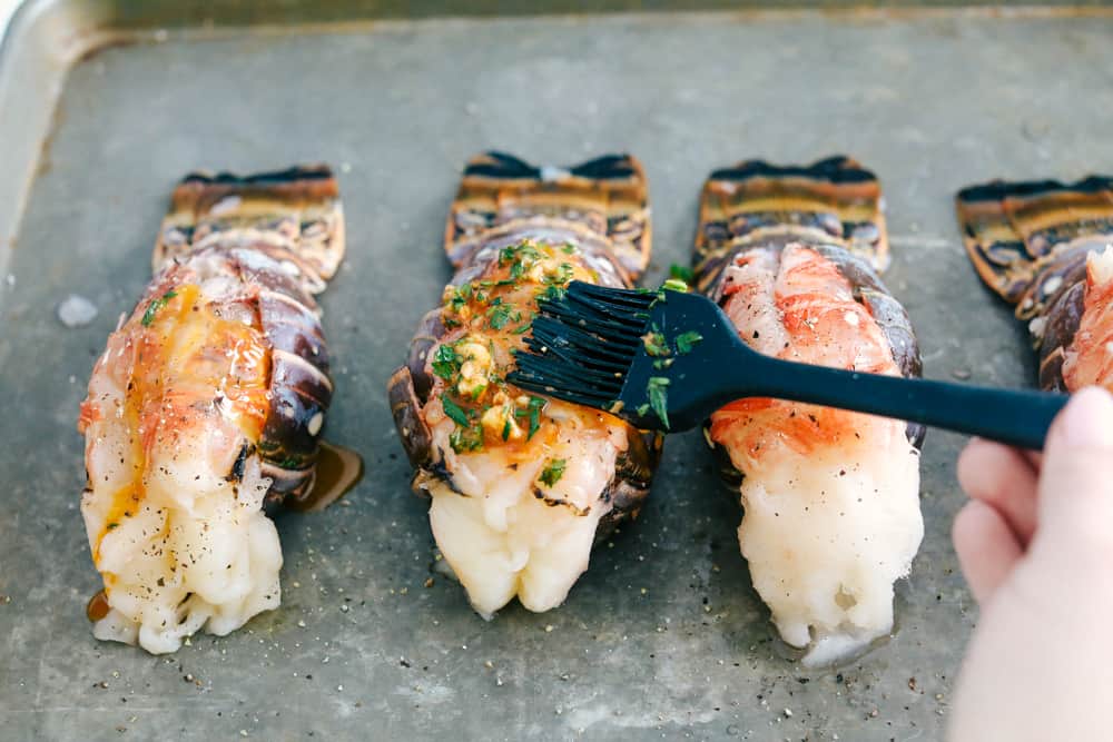 Spreading a buttery garlic herb sauce over top of the lobster tail. 