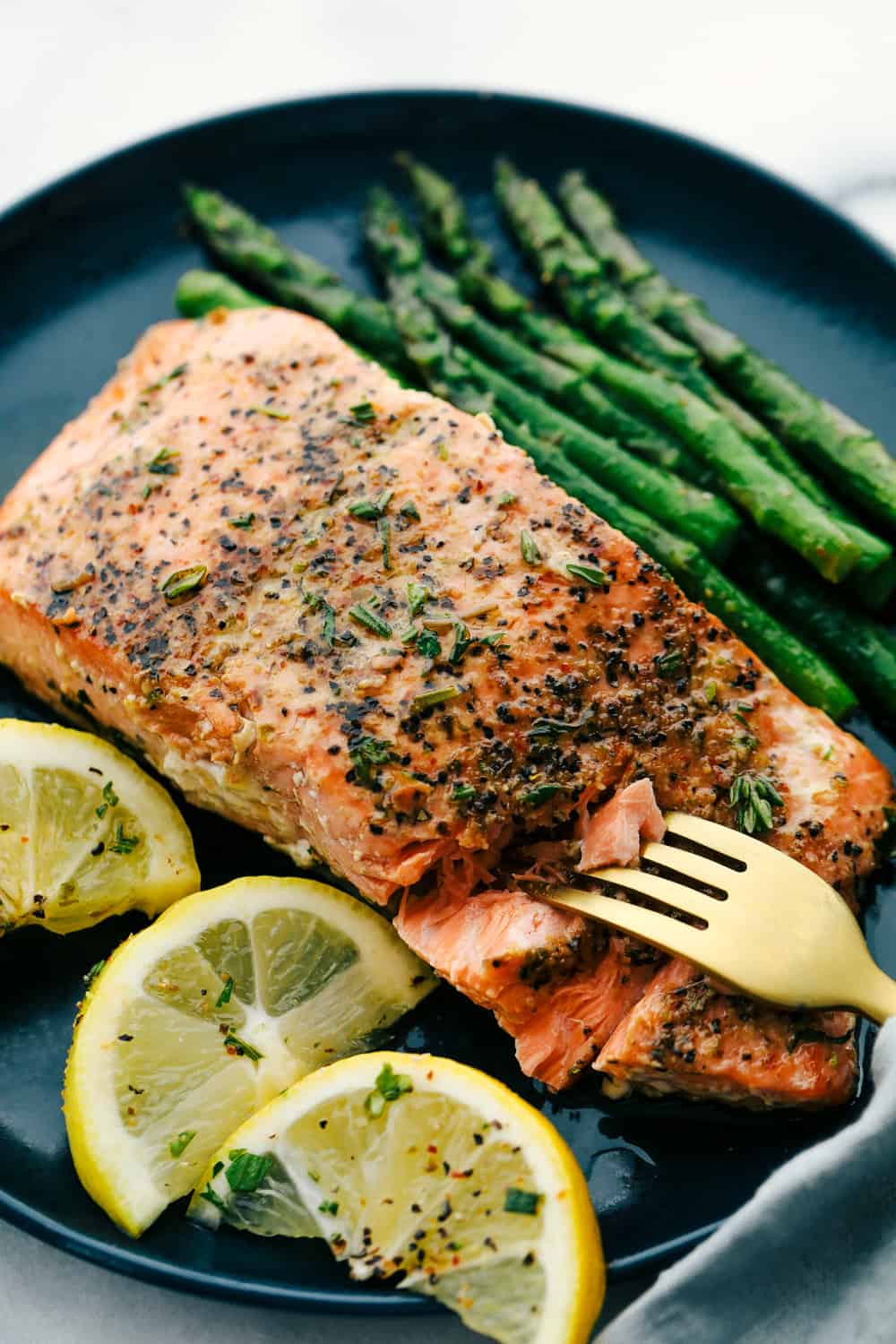 Brown butter lemon salmon on a plate with asparagus and lemon wedges. 