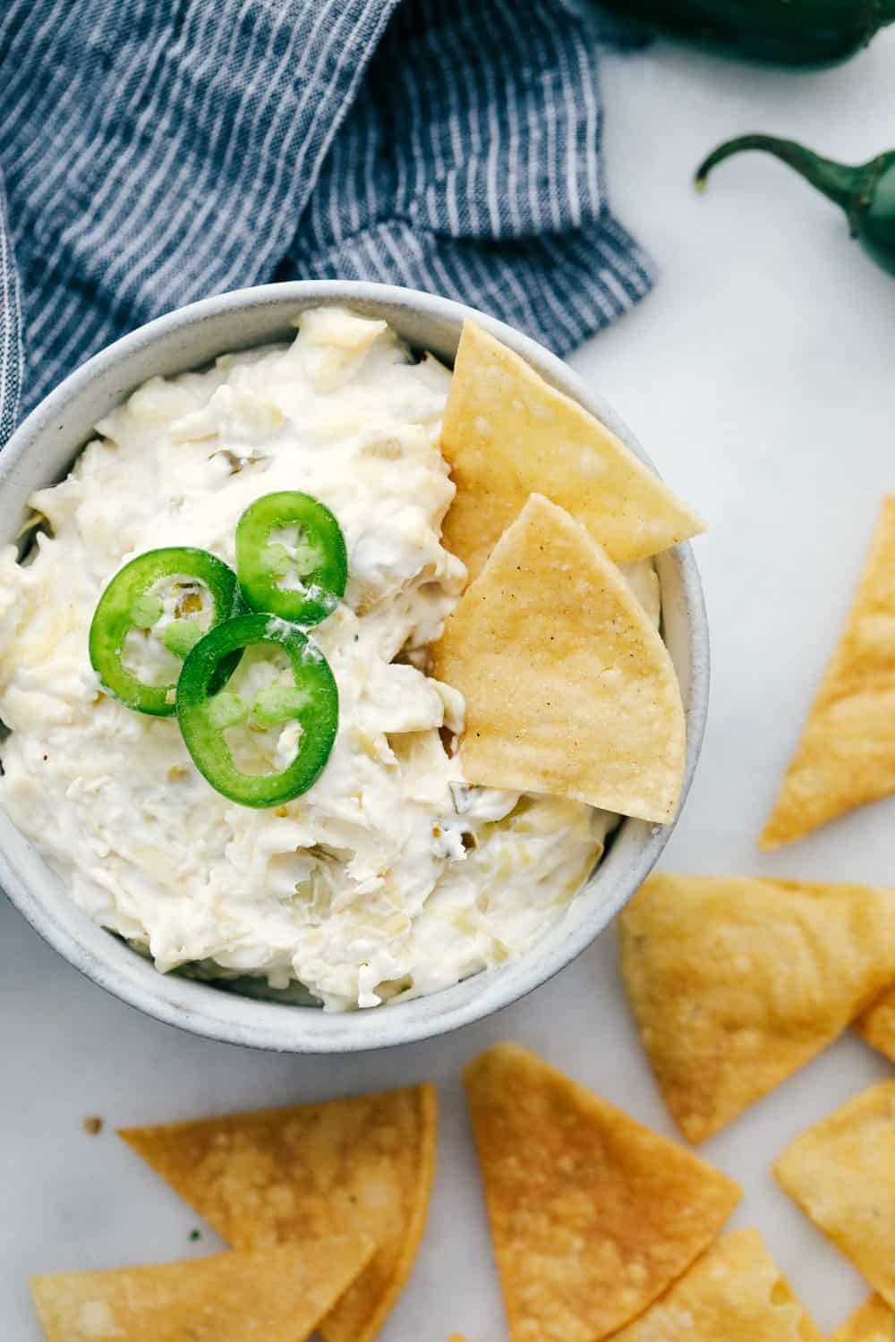 Jalapeño artichoke dip in a bowl with jalapeños garnished on top with chips for dipping.