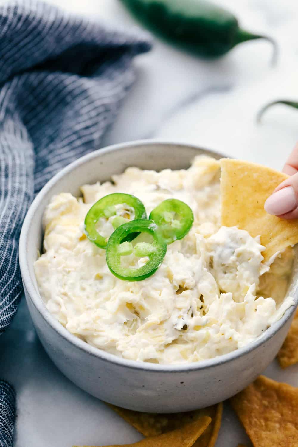 Jalapeno artichoke dip in a bowl garnished with jalapeños and a chip dipped in it. 
