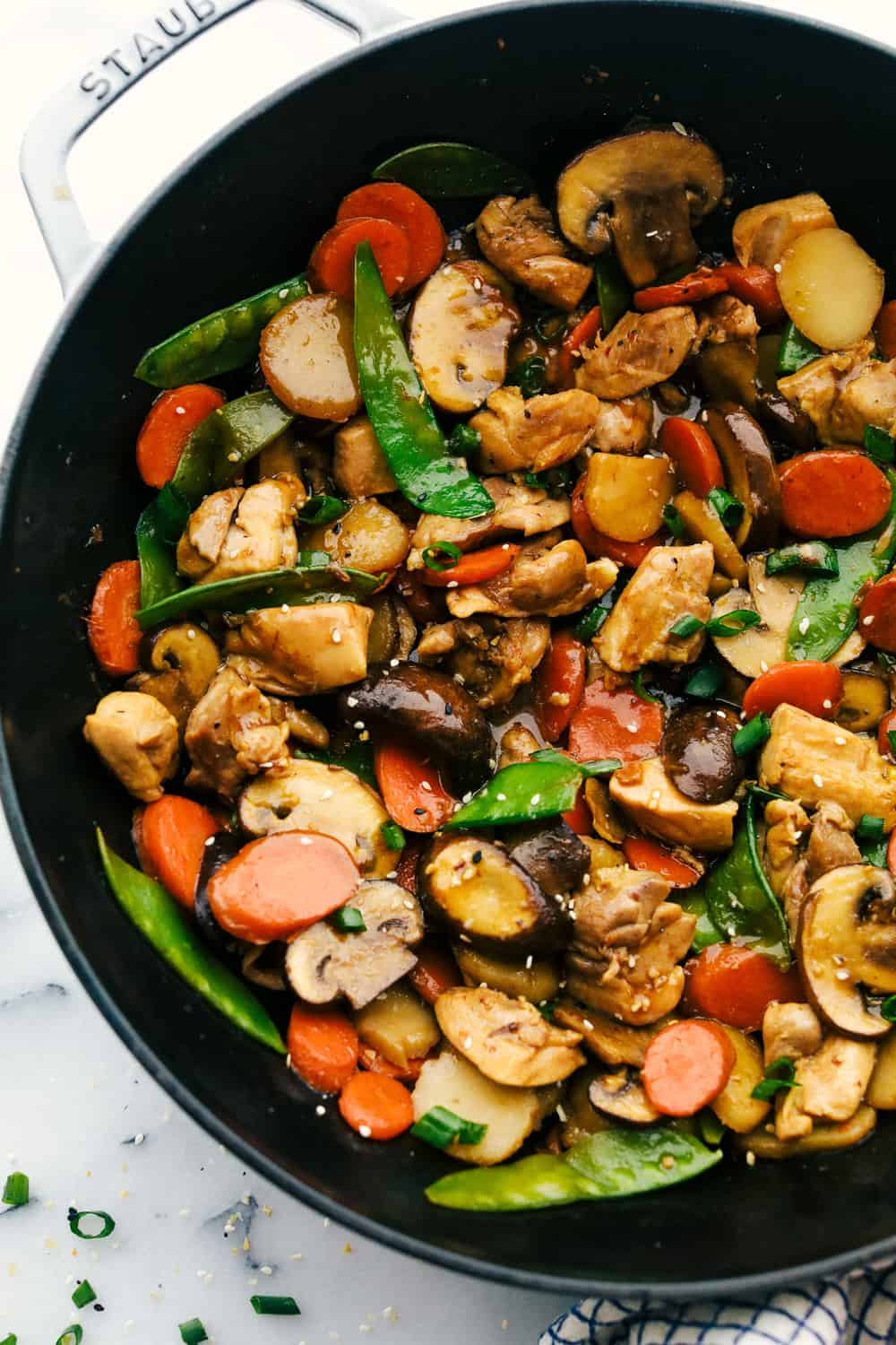 Moo Goo Gai Pan is a classic Chinese dish with tender chicken pieces and mushrooms then add in crisp vegetables such as carrots, water chestnuts, snow peas all stir fried together with a special white sauce poured over top and simmered all together. Way better than take out and only 20 minutes! Moo goo gai pan in a staub pan.